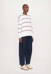 Hvit langermet skjorte med beige striper, denim vidde jeans og brune joggesko med subtile fargestriper. Enkelt design og avslappet passform.