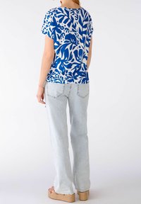 Kortærmet blå og hvid mønstret top med en løs pasform, parret med lyseblå lige jeans og beige kilehæle sandaler.