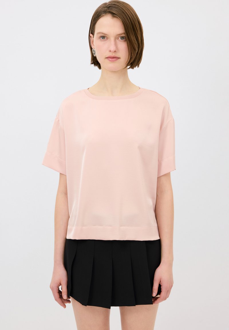 Top corto in satin rosa chiaro con maniche corte, scollo rotondo, forma boxy e orlo sotto la vita, abbinato a una gonna plissettata nera.