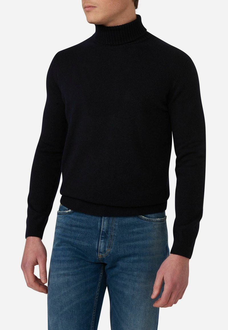 Schwarzer, gestrickter Rollkragenpullover mit geripptem Kragen und Bündchen, ergänzt durch ein figurbetontes Design. Kombiniert mit mittelblauen Jeans.