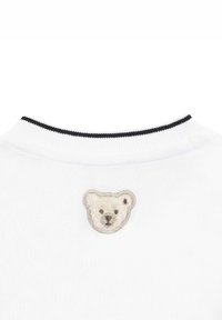 Cuello de sudadera blanca con bordado de una cara de oso texturizada en beige y detalles en marrón. Ribete de rayas en blanco y negro en el cuello.