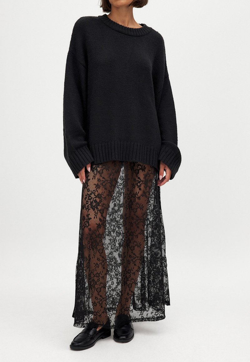 Oversized sort strikket sweater med ribbet kant parret med en transparent sort blonde nederdel med blomsterprint. Sorte sko fuldender looket.