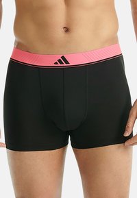 Svarta boxerkalsonger med resårband i rosa och svarta Adidas-logotyper och detaljer. Materialet är mjukt och åtsittande, vilket framhäver kroppens form.