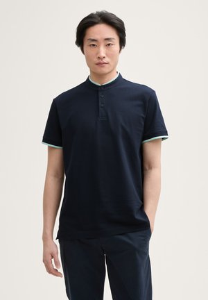 Polo shirt blu navy con colletto alto, tre bottoni e dettagli in azzurro chiaro a contrasto su colletto e maniche. Maniche corte, materiale in cotone.