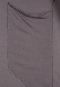 Grått tyg med en slät textur har en lappficka på vänster sida, utformad med rundade kanter och en overlock-söm.