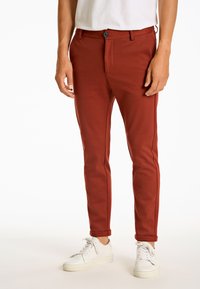 Rostfärgade tapered byxor med en mjuk textur, utrustade med knäppning, bälteslyor och uppvikt fåll, tillsammans med vita sneakers.