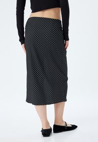 Jupe midi noire à pois, fabriquée en tissu doux, avec une taille cintrée et un léger ruché. Associée à des chaussures plates noires.