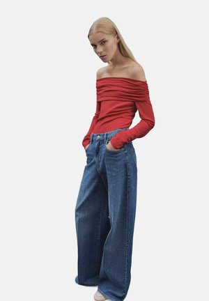 Cropped top rosso con scollo a bardot e maniche lunghe, adornato da dettagli arricciati, abbinato a jeans in denim blu a vita alta e gamba larga. Texture liscia e vestibilità rilassata.