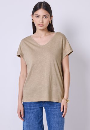 Lys beige v-hals t-shirt med rullede korte ærmer, blød tekstur, afslappet pasform, parret med blå løst siddende jeans. Enkel design, uden mønstre.