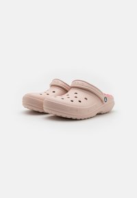 Clogs Crocs rose clair en matériau flexible, dotés de trous de ventilation, d'une sangle à l'arrière et de semelles texturées pour une bonne adhérence.