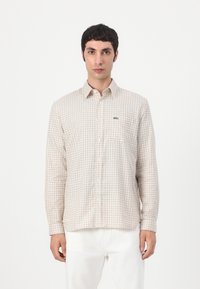 Beige button-up shirt with a grid pattern in brown, featuring a chest pocket and a small green logo on the left side. Long sleeves.