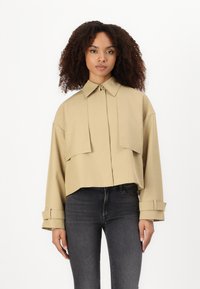 Chemise cropped kaki avec un col structuré, coupe oversized et deux poches à rabat sur le devant. Manches longues avec détails aux poignets.
