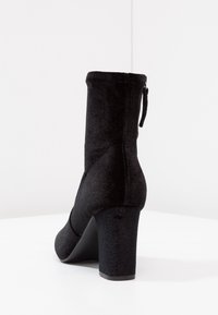 Bottine noire à finition texturée, bout rond et talon épais. Dotée d'une fermeture éclair latérale et d'une tige lisse et ajustée.