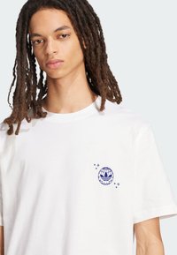 Bijela pamučna majica s plavim globus logom i tri pruge na lijevom prsnom dijelu, kratkih rukava i klasičnim okruglim izrezom.