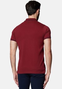 Bordowa koszulka polo z klasycznym kołnierzykiem, krótkimi rękawami i paskowanymi akcentami na mankietach. Wykonana z bawełny, o gładkiej teksturze.