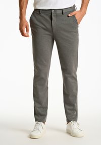 Grijze, slim-fit broeken van gestructureerde stof, met een knoopsluiting en zijzakken, gecombineerd met witte sneakers.