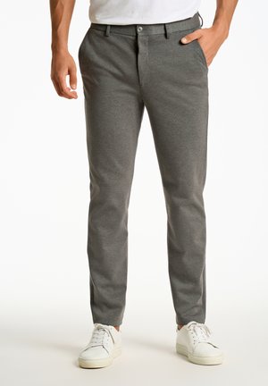 Szare, slim-fit spodnie wykonane z teksturowanej tkaniny, z zapięciem na guziki i bocznymi kieszeniami, zestawione z białymi trampkami.