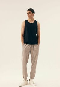 Black sleeveless tank top, light grey tapered pants, white sneakers. Fabric appears smooth, with elastic waistband and side pockets.