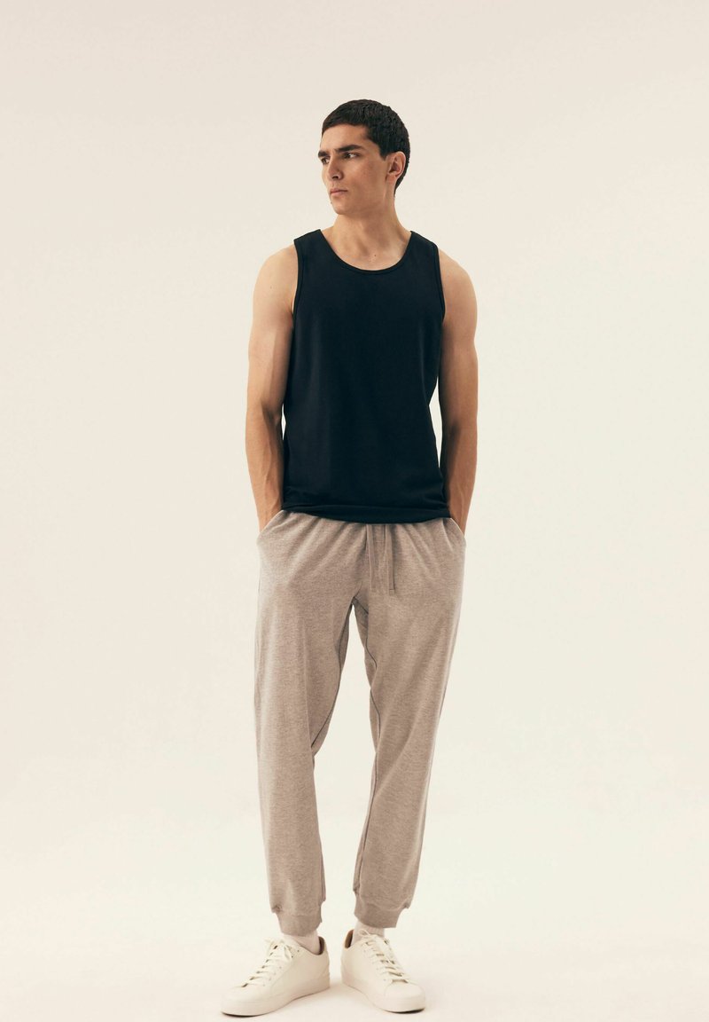 Black sleeveless tank top, light grey tapered pants, white sneakers. Fabric appears smooth, with elastic waistband and side pockets.