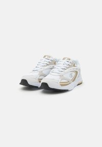 Scarpe sportive bianche con tomaia in rete, dettagli dorati e suola in gomma nera. Presentano lacci e un colletto imbottito per supporto e comfort.
