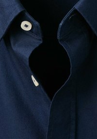 Camicia blu navy con bottoni, caratterizzata da un colletto classico, due bottoni bianchi e un tessuto resistente. La scollatura presenta un'apertura a chiave.
