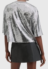 Top in paillettes argento con design corto, maniche corte e una texture liscia, abbinato a una gonna in pelle nera.