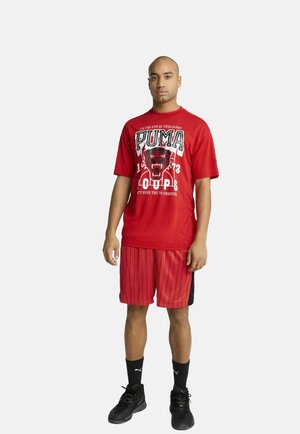 Red short-sleeve t-shirt with a black graphic design featuring a panther, paired with red and black striped basketball shorts, black sneakers.