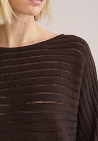 Pull en maille à rayures marron avec des lignes texturées horizontales et verticales. Encolure large et tissu doux et respirant.