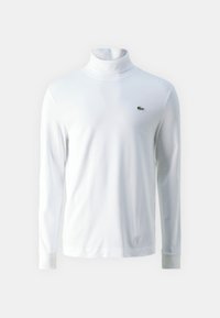 Chemise à col roulé blanche à manches longues en tissu doux, ornée d'un petit logo brodé vert sur la poitrine et de poignets ajustés.