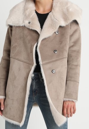 Beige faux fur coat with a wide collar, double-breasted design, and textured fabric. Features snap buttons and a soft white trim.