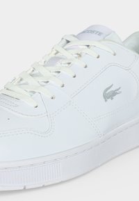 Λευκό sneaker Lacoste με λευκά κορδόνια, υφασμένο πέλμα και γκρι λογότυπο κροκόδειλου στο πλάι.