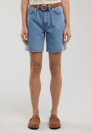 Shorts en denim bleu clair avec une taille haute, des ourlets retroussés et des coutures visibles. Portés avec une ceinture marron et une coupe décontractée.