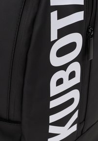 Czarny plecak z teksturowanego materiału, z wyraźnym białym napisem. Posiada zamek błyskawiczny i minimalistyczny design dla funkcjonalności.