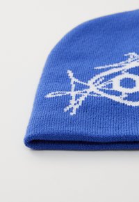 Blauwe gebreide beanie met een geribbelde textuur, voorzien van een wit geometrisch patroon aan de voorkant en een omgeslagen rand aan de onderkant.
