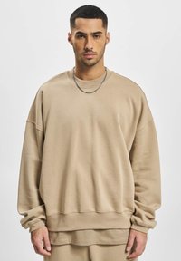 Beige oversized sweatshirt made of soft-textured fabric. Features a round neck, dropped shoulders, and ribbed cuffs and hem.