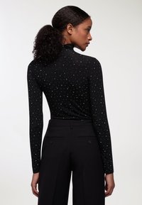 Maglia nera a maniche lunghe con colletto alto, decorata con punti argentati, abbinata a pantaloni neri a vita alta con tasche laterali.