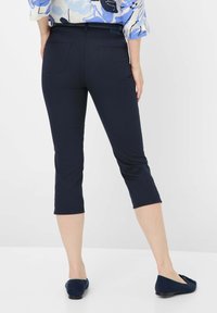 Pantaloni capri blu navy con design aderente, materiale elasticizzato e due tasche posteriori. Indossati con ballerine blu scure.
