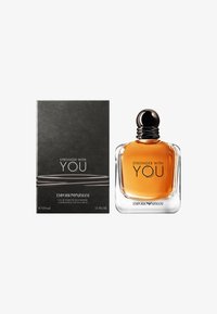 Parfymflaska med en rektangulär glasdesign, bärnstenfärgad vätska, svart rundad kork; åtföljd av en svart låda med silvertext.