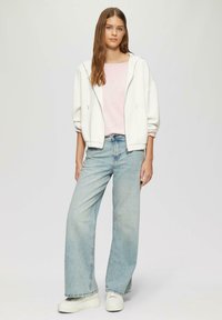Sweat à zip blanc, haut rose clair, jeans large bleu clair et baskets blanches encombrantes. Textures douces, coupe décontractée, style décontracté.