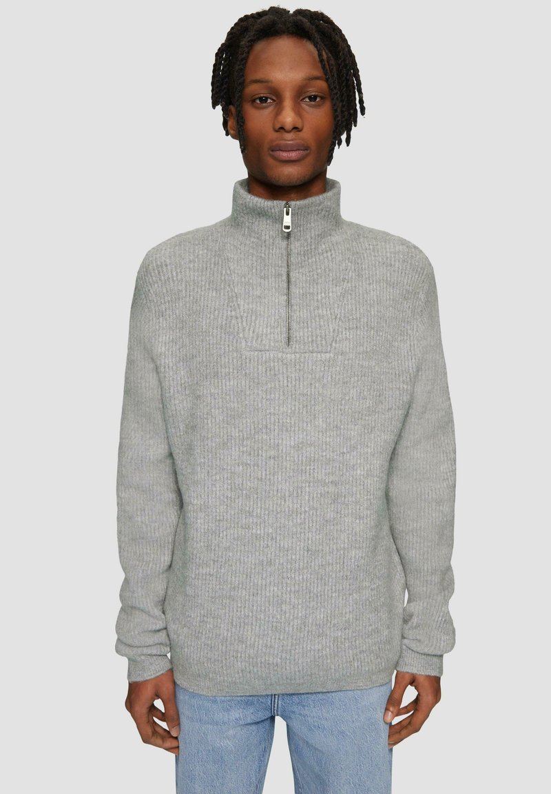 Grauer gestrickter Pullover mit hohem Kragen und einem Viertelreißverschluss. Hat ein strukturiertes Rippmuster und lange Ärmel. Wird über hellblauen Jeans getragen.