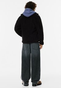 Czarna polarowa kurtka z niebieską bluzą wystającą spod spodu, w połączeniu z szerokimi ciemnoniebieskimi dżinsami, pokazana z tyłu.