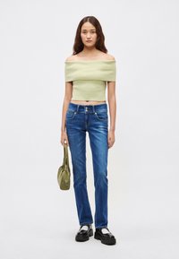 Svetlo zelena rebrasta kratka majica z odkrytimi rameni, modre kavbojke z ravnimi nogavicami, črni platformni čevlji in mala zelena ročna torbica.