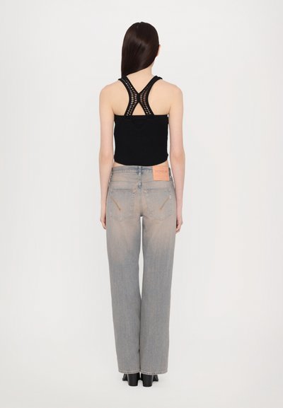 Top cropped de malha preta com alças cruzadas nas costas, combinado com jeans de perna larga de cintura alta em azul claro, featuring um patch da marca em rosa. Textura de tecido suave.