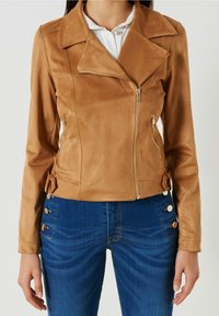 Pískově hnědá koženka bunda s diagonálním zipem, klopovým límcem a postranními zipy. Stylizováno s akcentovými knoflíky na manžetách a pase.