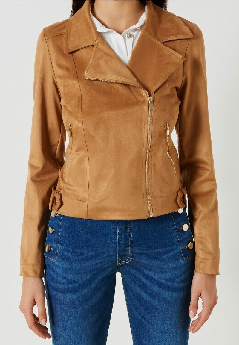 Pískově hnědá koženka bunda s diagonálním zipem, klopovým límcem a postranními zipy. Stylizováno s akcentovými knoflíky na manžetách a pase.