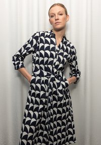 Navyblaues und weißes gemustertes Kleid aus Stoff, mit Knopfverschluss vorne, Kragen, langen Ärmeln und tailliertem Bund mit Taschen.