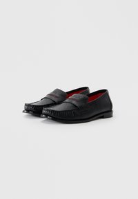 Sorte loafers lavet af tekstureret læder med glatte accenter. Har en rund tå, syningsdetaljer og en kontrasterende rød inderside.