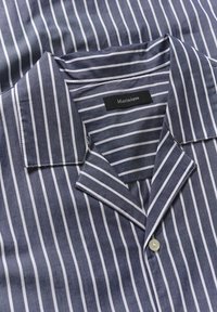 Kék és fehér, függőlegesen csíkozott, galléros ing gyöngygombbal és látható márkacímkével a gallér belső részén.