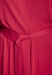 Haljina do koljena, u stilu omota, od svijetloroze tkanine s glatkom teksturom, s odgovarajućim remenom i naboranim detaljima.