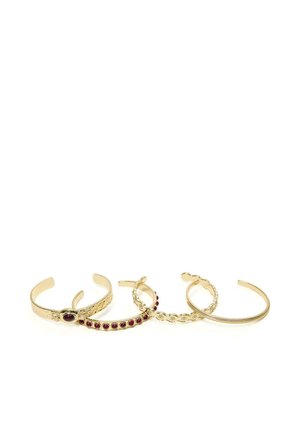 Fire guldfarvede manchetarmbånd, to med røde ædelstene, hver med unikke indgraverede og perlebesatte designs, vist på hvid baggrund.